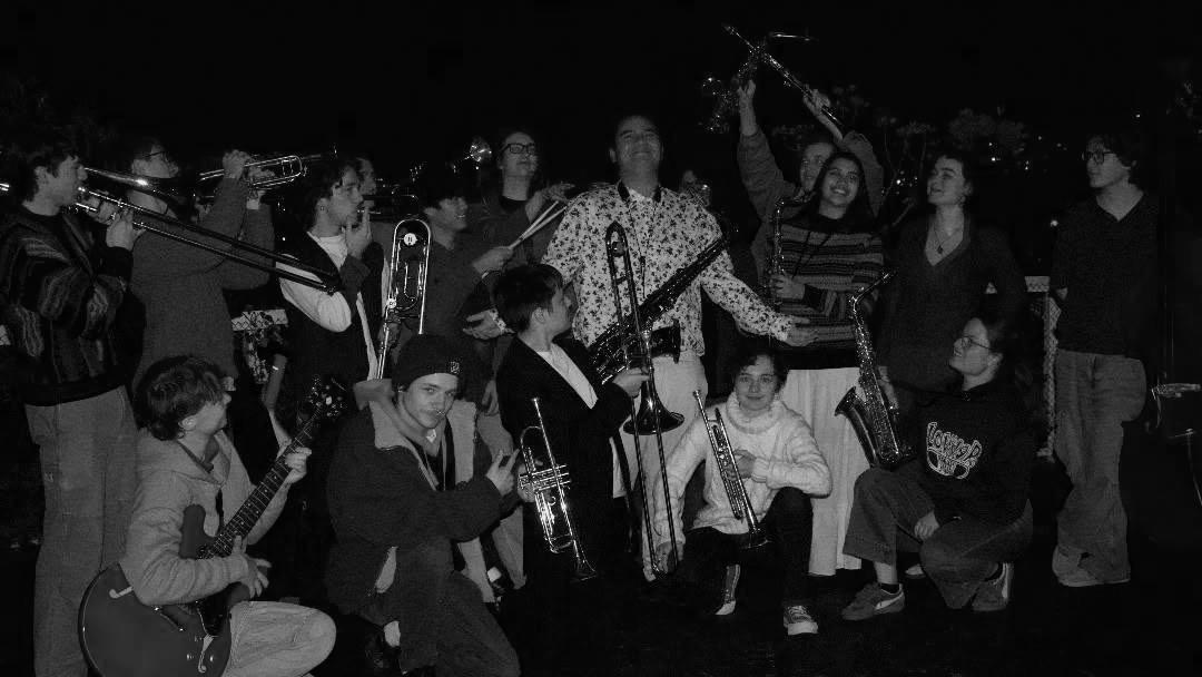 A large group of big band musicians pose candidly together with their brass instruments 