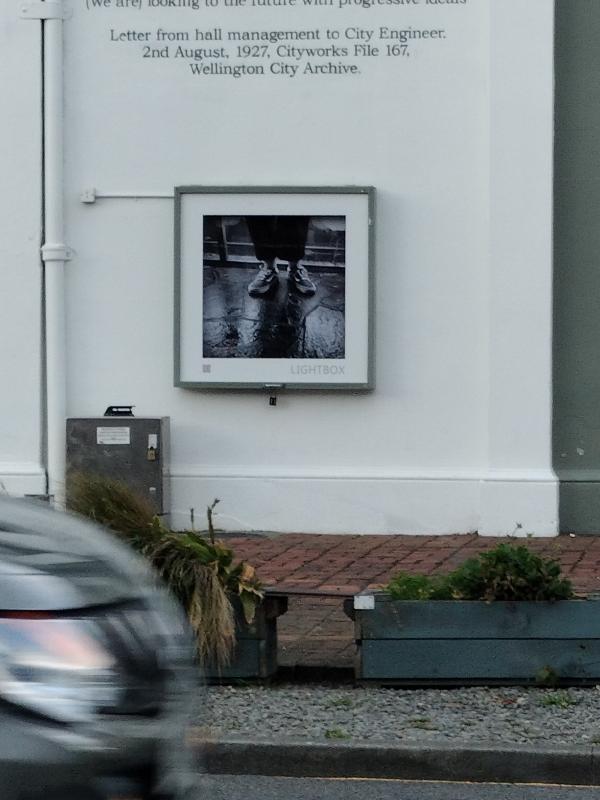 Izakaya Kabu (居酒屋かぶ), a black and white photograph of feet on wet concrete by Tiso Ross sits in the Thistle Hall Lightbox