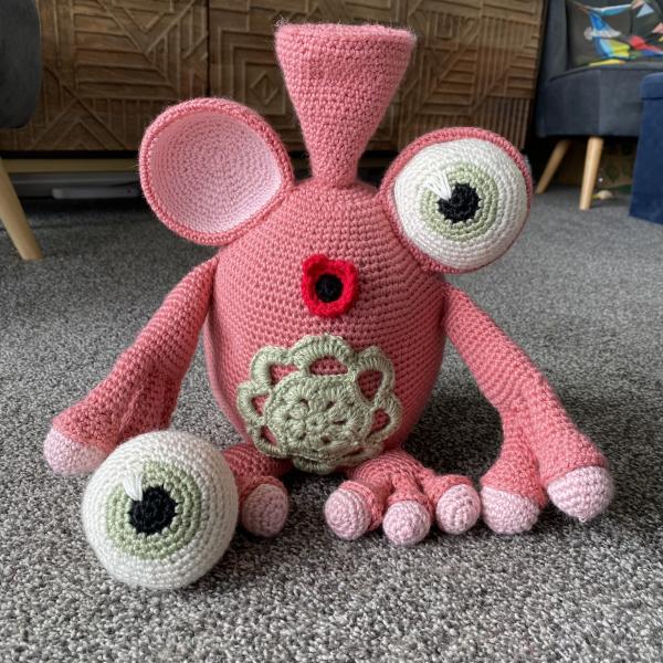 knitted pink creature with an eye on the floor