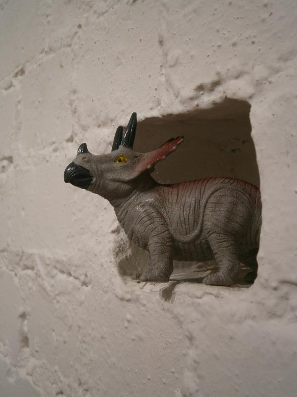 Installation from 'Plastic Fantastic' exhibition by Hilary Unwin. A toy triceratops gazes wistfully from a nook in a brick wall.